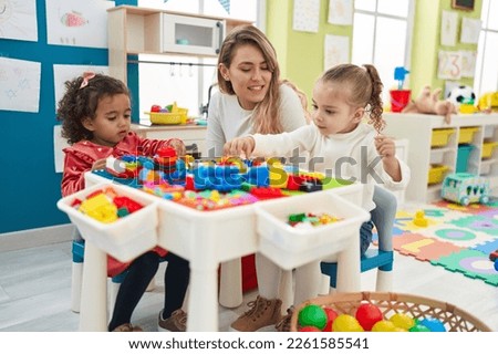 Teacher with girls playing with construction blocks sitting on table at kindergarten