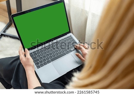 young girl holds a laptop looking at a mock up of a green computer screen online PC training, watching a movie. Close-up view over the shoulder