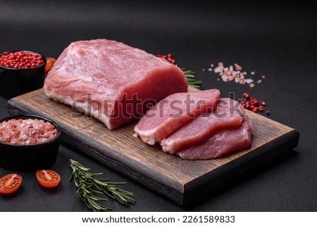 A piece of raw fresh pork on a wooden cutting board with spices and herbs on a dark concrete background Royalty-Free Stock Photo #2261589833