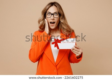 Young employee business woman corporate lawyer wear classic formal orange suit glasses work in office hold gift certificate coupon voucher card for store hold face isolated on plain beige background