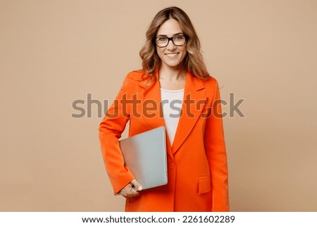 Young happy successful employee IT business woman corporate lawyer 30s wear classic formal orange suit glasses work in office hold closed laptop pc computer isolated on plain beige background studio