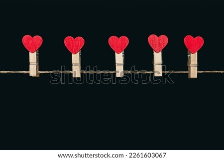 Clothespins decorated with red hearts hang on a rope on a black background. Concept for lovers. Valentine's Day holiday. Decor in the form of clothespins and free space for the designer
