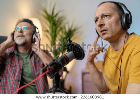 Two mature podcasters and having a good time in a studio. Two happy men co-hosting a live audio broadcast. Two male content creators recording an internet podcast. check the sound quality