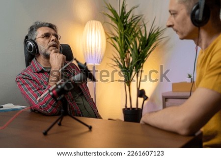 two cheerful radio hosts in headphones recording podcast in studio together. Happy male podcasters having a great conversation on an audio broadcast in a home studio. broadcasting at home office 