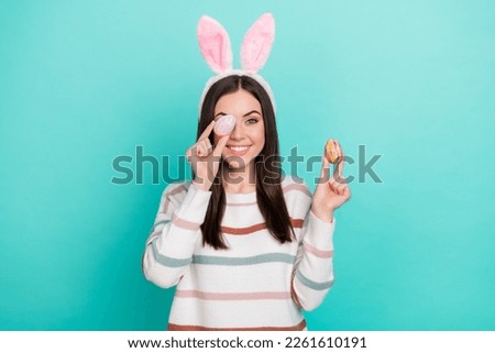 Photo of funny lady hold easter eggs cover eye beaming smile wear rabbit ears striped sweater isolated blue color background