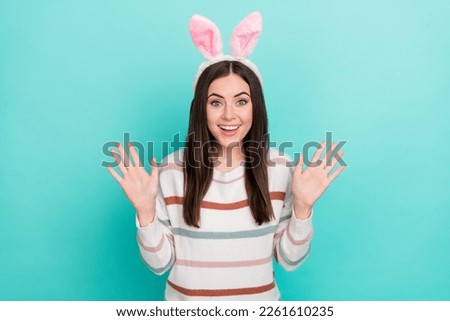 Photo of excited pretty woman wear striped sweater bunny headband rising arms isolated turquoise color background