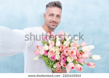 man with valentines tulips making selfie in studio. man with valentines tulips isolated on blue