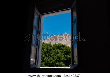 Looking through a window at a tree and hill on the greek island of Santorini during the day