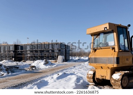 A bulldozer on a construction site in winter against the background of modular buildings. Construction industry concept Royalty-Free Stock Photo #2261636875
