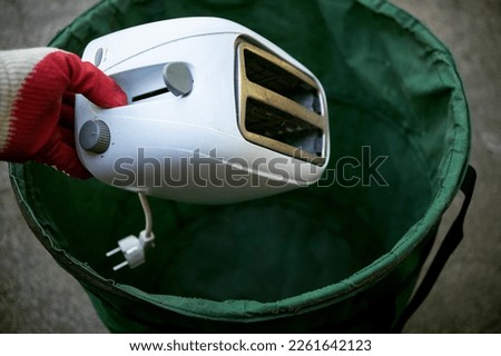 Throw old household appliances in the trash.A hand throws a sandwich toaster into a bucket.Disposal of kitchen appliances. Royalty-Free Stock Photo #2261642123