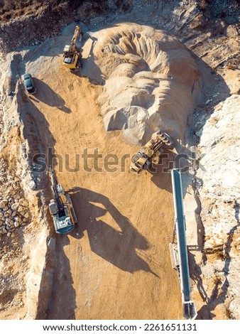 Vertical photo of yellow heavy machinery, excavators working on dusty quarry grounds 