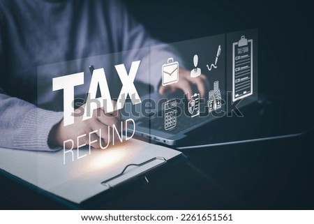 Businessman using a pen to write a notebook with TAX REFUND and refund tax of duty taxation business, graphs and chart being demonstrated on the screen media,  tablet pc and selecting tax refund. Royalty-Free Stock Photo #2261651561