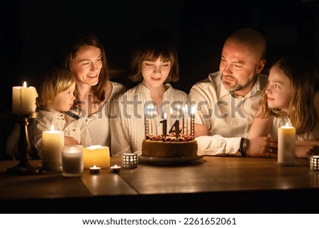 Cute fourteen years old girl making a wish before blowing candles on her birthday cake. Family of five celebrating childs birthday. Birthday traditions.