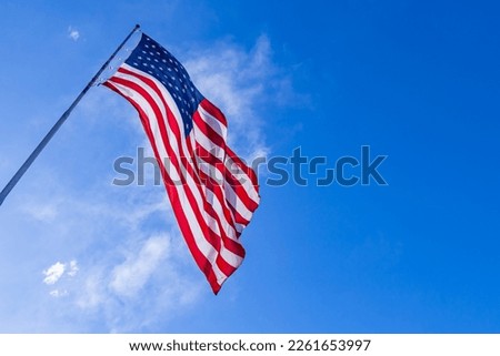 Close up of large American flag waving in front of blue sky and white cloud. American Flag waving in wind. Close up of United States flag. American Flag Waving Under A Blue Sky With Clouds.