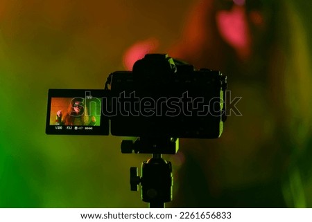 Backstage how operator working with professional camera. Videographer shoots music clip with actress or singer celebrity woman in dark studio with neon color light. High quality photo