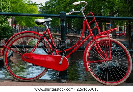 A parked red bicycle chained to a railing on a bridge over a canal in Amsterdam during the summer