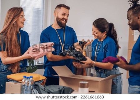 Group of multiracial volunteers helping people at charity center. Humanitarian aid concept. Bearded man and his colleagues working in homeless shelter and packing clothes into donation boxes. Royalty-Free Stock Photo #2261661663