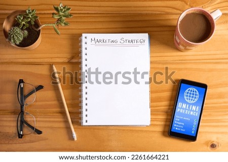 Top view of marketing strategy text on blank notebook page and mobile phone with online presence report on wooden table with pencil, eyeglasses, succulent plant and cup of coffee. Planning mockup.