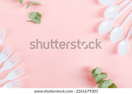 White plastic forks, spoons and green sprouts lie on the sides on a light pink background with copy space for your text in the center, flat lay close-up. The concept of ecology, plastic garbage dispos