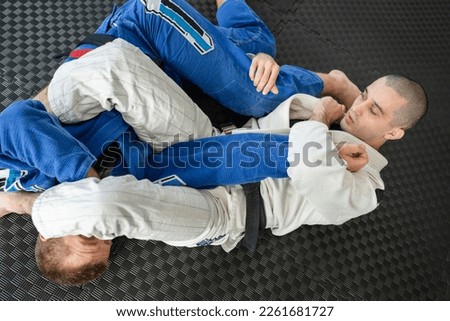 Brazilian jiu jitsu bjj training or sparing two athletes fighters dill martial arts technique at gym on the tatami mats wear kimono gi black belt instructor demonstrate submission armbar juji gatame Royalty-Free Stock Photo #2261681727