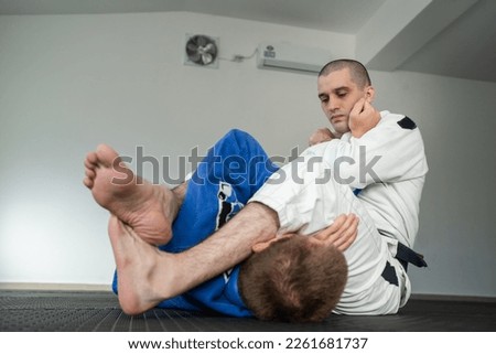 Brazilian jiu jitsu bjj training or sparing two athletes fighters dill martial arts technique at gym on the tatami mats wear kimono gi black belt instructor demonstrate submission armbar juji gatame Royalty-Free Stock Photo #2261681737