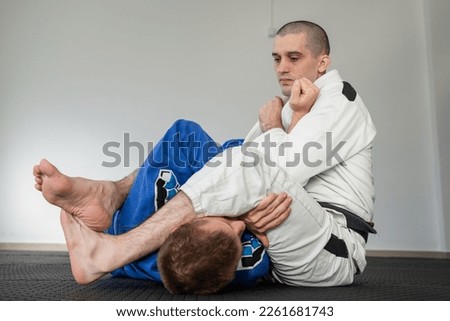 Brazilian jiu jitsu bjj training or sparing two athletes fighters dill martial arts technique at gym on the tatami mats wear kimono gi black belt instructor demonstrate submission armbar juji gatame Royalty-Free Stock Photo #2261681743