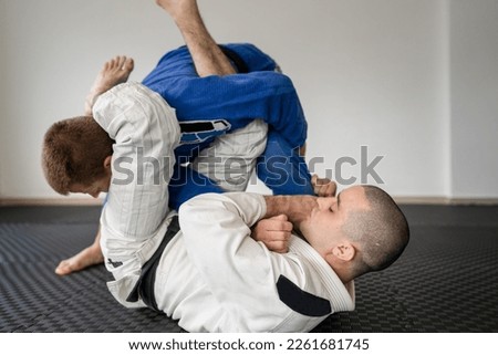 Brazilian jiu jitsu bjj training or sparing two athletes fighters dill martial arts technique at gym on the tatami mats wear kimono gi black belt instructor demonstrate submission armbar juji gatame Royalty-Free Stock Photo #2261681745