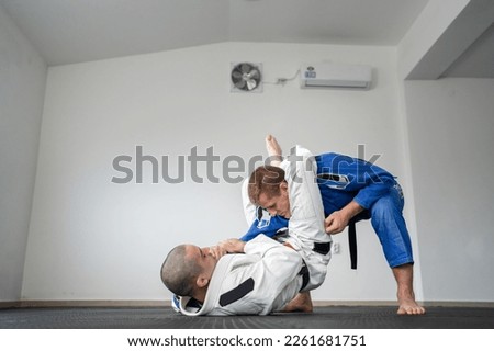Brazilian jiu jitsu bjj training or sparing two athletes fighters dill martial arts technique at gym on the tatami mats wear kimono gi black belt instructor demonstrate submission triangle Royalty-Free Stock Photo #2261681751