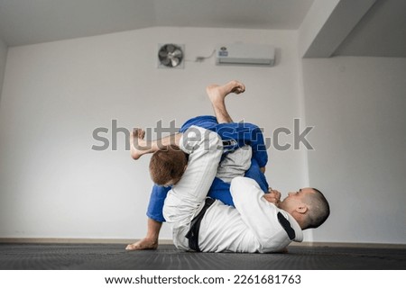 Brazilian jiu jitsu bjj training or sparing two athletes fighters dill martial arts technique at gym on the tatami mats wear kimono gi black belt instructor demonstrate submission armbar juji gatame Royalty-Free Stock Photo #2261681763