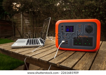 Portable power station solar electricity generator outdoors with laptop plugged in charging. Wireless charging lithium battery backup for power outage emergencies outdoors, camping or travel. Royalty-Free Stock Photo #2261681909