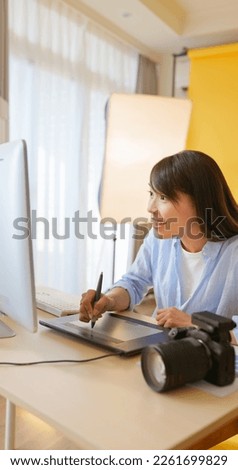 asian female photographer with digital camera is using graphics tablet and laptop computer in studio