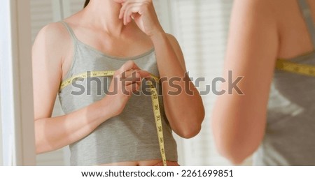 asian unhappy woman is dissatisfied while she measuring her chest and breast in front of mirror Royalty-Free Stock Photo #2261699851