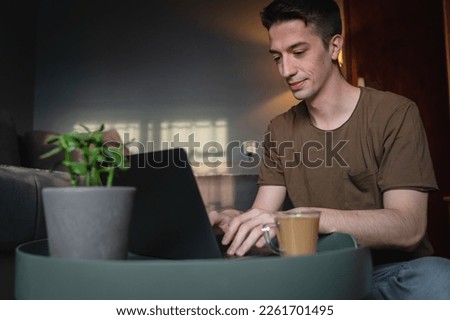 A young guy is using his laptop computer at home for business or studying in his room during the day with coffee on table and mobile phone