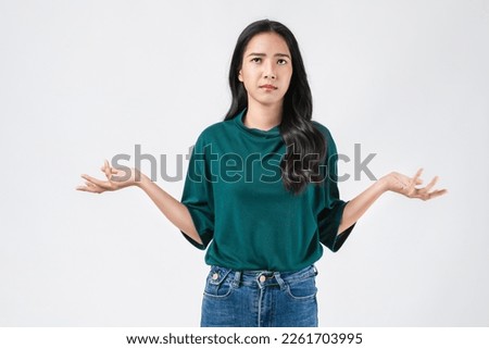 Confused young woman wearing casual green t-shirt and shrugging shoulders, isolated on white background. Royalty-Free Stock Photo #2261703995