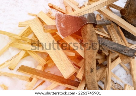 an axe and firewood in the snow, a finely chopped wooden log for heating the house in the absence of gas heating, solar glare, selective focus. High quality photo