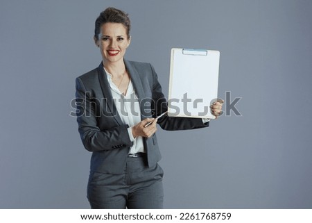 happy elegant small business owner woman in grey suit with clipboard isolated on grey background. Royalty-Free Stock Photo #2261768759