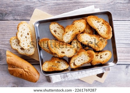 Crostini, Crusty baguette slices toasted with olive oil, on a baking tray. Top view. Royalty-Free Stock Photo #2261769287