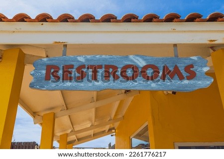 Close-up view of Restroom sign under roof of yellow building. Aruba. 