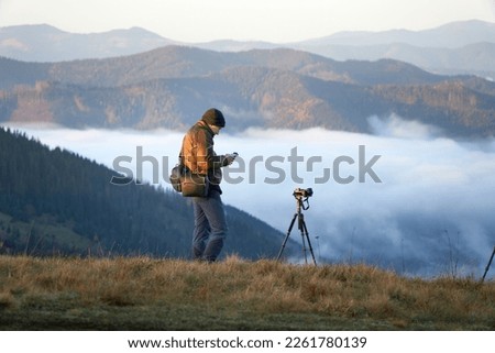 Photographer working outdoor. Taking photos in mountains. Nature photographer in action. Silhouette of a landscape photographer in twilight.