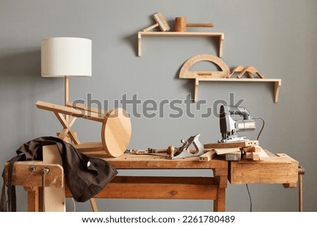 Background image of carpenters workstation, carpenters work table with different tools, wood cutting, a jigsaw, a cipher machine, and a chair made in a carpentry workshop. Royalty-Free Stock Photo #2261780489