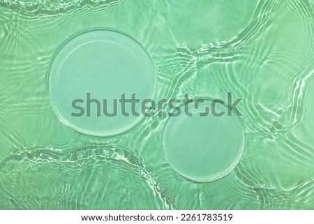 Two empty clear glass circle podiums on green transparent calm water texture with waves in sunlight. Abstract nature background for product presentation. Flat lay cosmetic mockup, copy space.