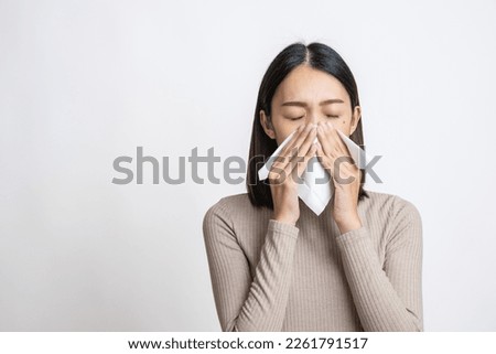 Portrait of beautiful young asian sick woman over isolated white background being wrapped in scarf sneezing, suffering from runny nose and high temperature. Cold and fever concept. Royalty-Free Stock Photo #2261791517