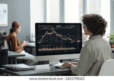 Young female stock exchange manager analyzing online statistic data while sitting in front of desktop computer screen in openspace office Royalty-Free Stock Photo #2261798321