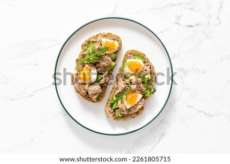 Tuna toast. Open sandwiches with whole grain bread, canned tuna, boiled egg, avocado and arugula. Top view Royalty-Free Stock Photo #2261805715