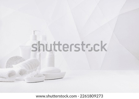 Cosmetic products in white bottles and toiletry - towels, bath salt, sponge for hygiene, cleansing, body care in soft light white interior with lines, polygons in geometric modern style, copy space.
