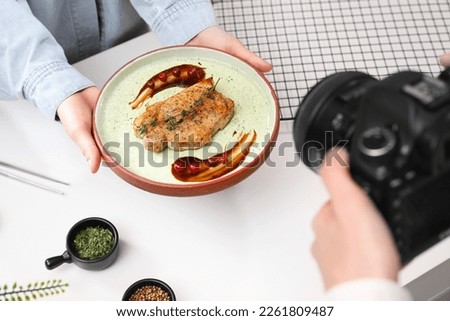 Food stylist holding plate with delicious meat medallion while photographer taking photo in studio, closeup