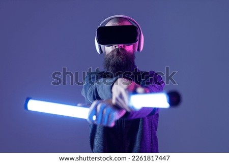 Young man in futuristic costume on dark background. Guy using VR helmet. Augmented reality, virtual reality, future technology, game concept. Blue neon light. 