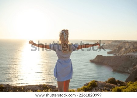 The back view of the traveller's girl who dmires the nture of the rocks, sun and water. the tourist woman is dressed in summer clothes, blue sundress Royalty-Free Stock Photo #2261820999