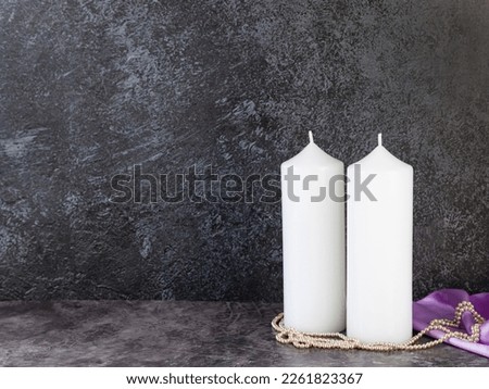 Decorative candles on lilac satin with flowers and beads on a dark marble background.