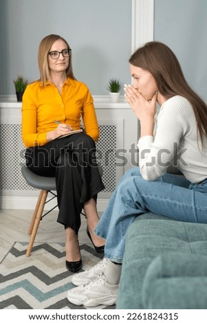 Counseling on depression, apathy. Young woman tells a psychologist about her life, she is sad, she put her hands to her face. Focus on the psychologist. Vertical photo